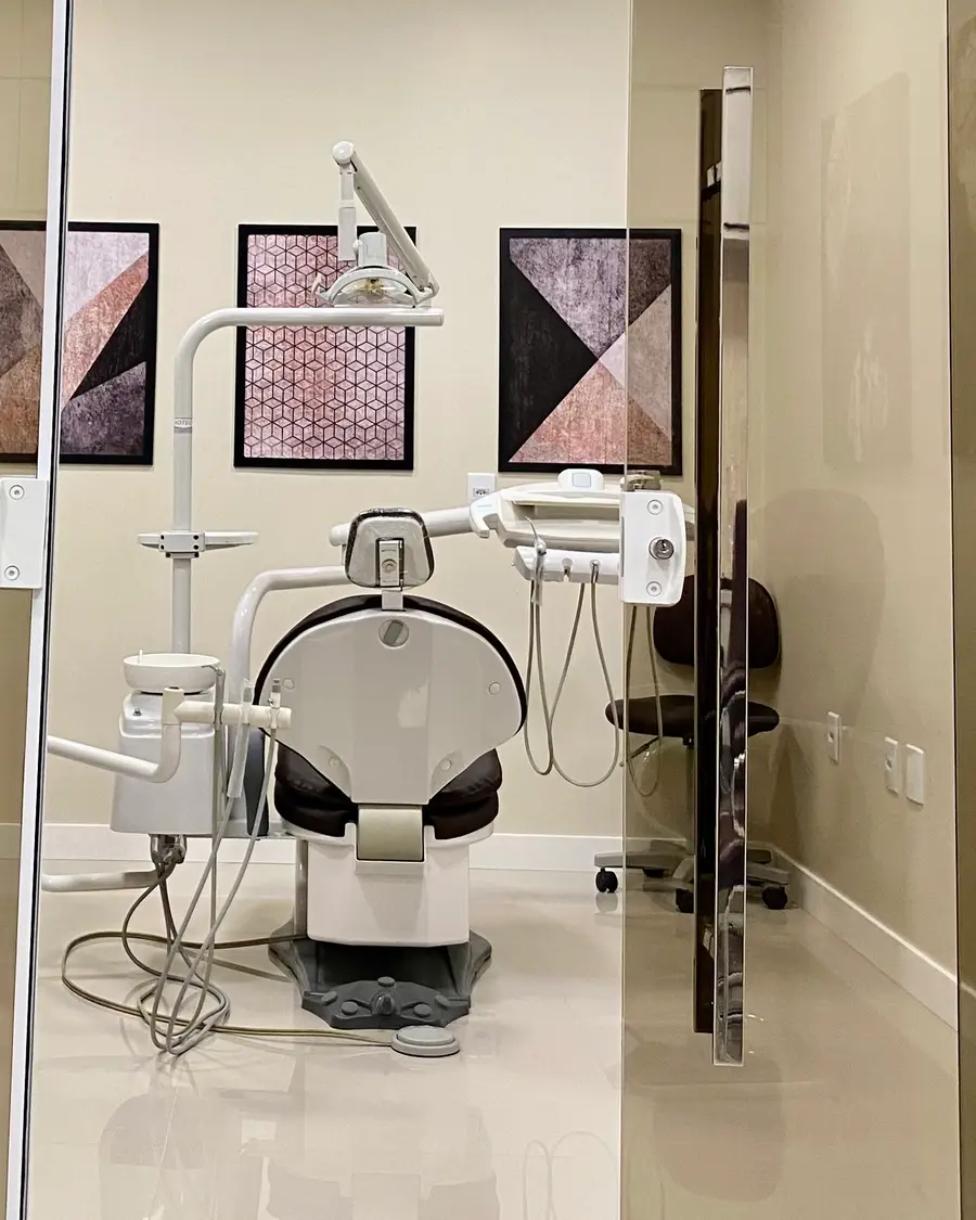 Consultório visto pela porta de vidro, com a cadeira odontológica e quadros na parede